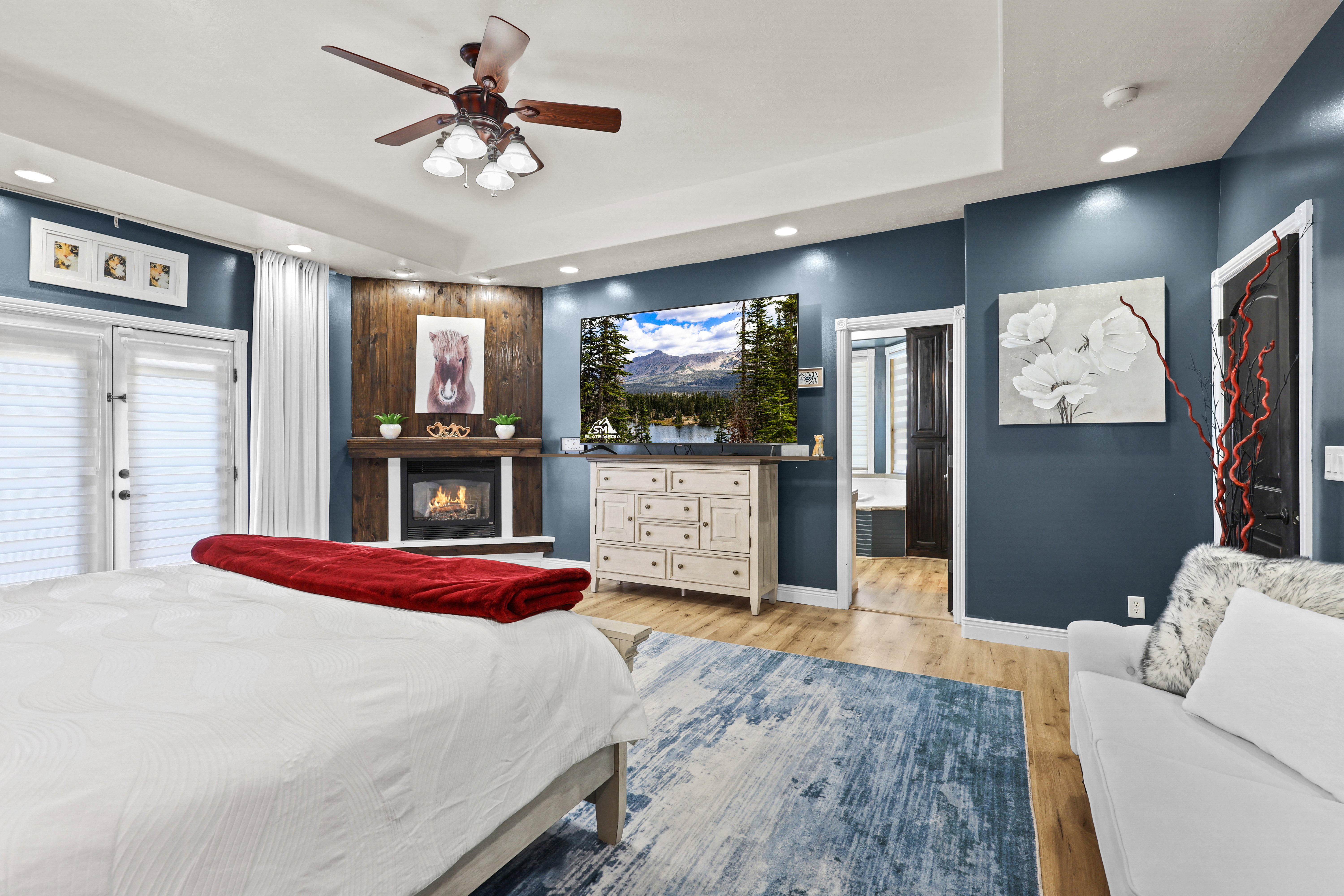 Bedroom with recessed lighting, light wood finished floors, a ceiling fan, a glass covered fireplace, and a raised ceiling