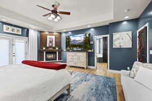 Bedroom with recessed lighting, light wood finished floors, a ceiling fan, a glass covered fireplace, and a raised ceiling