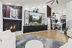 Living room with a fireplace, light wood-style floors, ceiling fan, and lofted ceiling