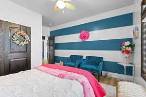 Bedroom with wood finished floors, a ceiling fan, a closet, and an accent wall