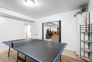 Rec room with light wood-style floors and a textured ceiling
