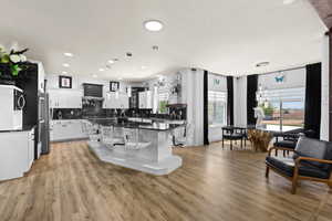 Kitchen with a kitchen island, white cabinets, tasteful backsplash, pendant lighting, and light wood finished floors