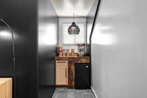 Kitchen featuring refrigerator, black fridge, a textured ceiling, pendant lighting, and light wood finish cabinetry
