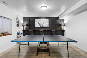 Recreation room with light wood-type flooring and a textured ceiling