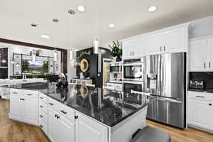 Kitchen with white cabinets, stainless steel appliances, dark stone counters, decorative light fixtures, and light wood-style flooring
