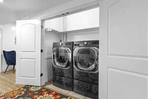 Laundry area with washer and clothes dryer and light wood-style flooring