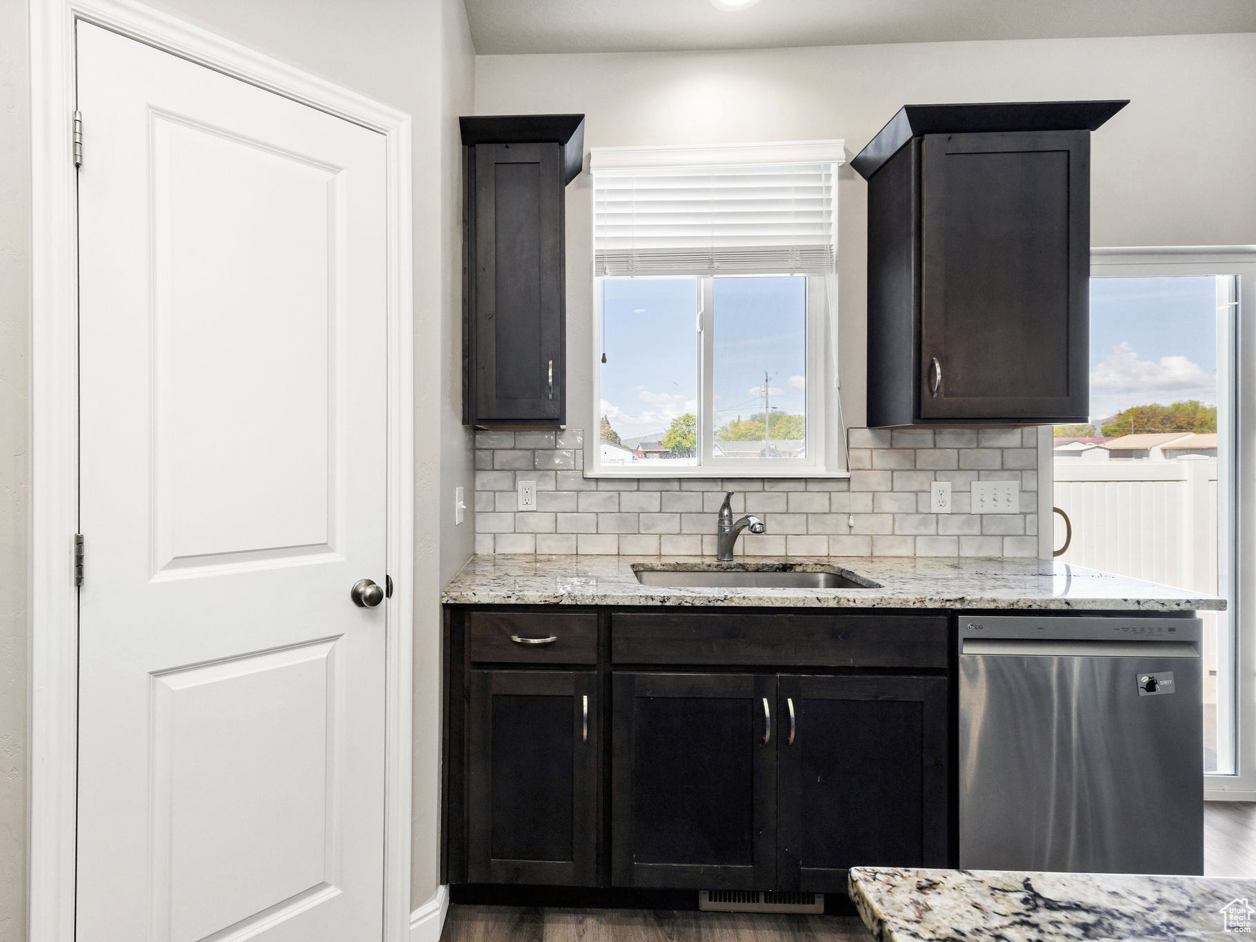 Kitchen with light stone countertops, backsplash, dishwasher, and dark wood-style floors