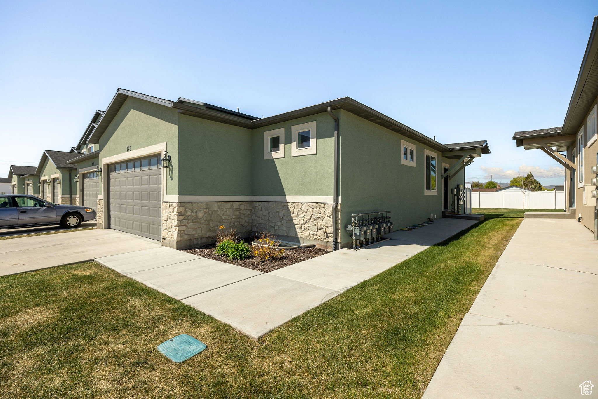 View of side of property with an attached garage, stucco siding, driveway, stone siding, and a lawn
