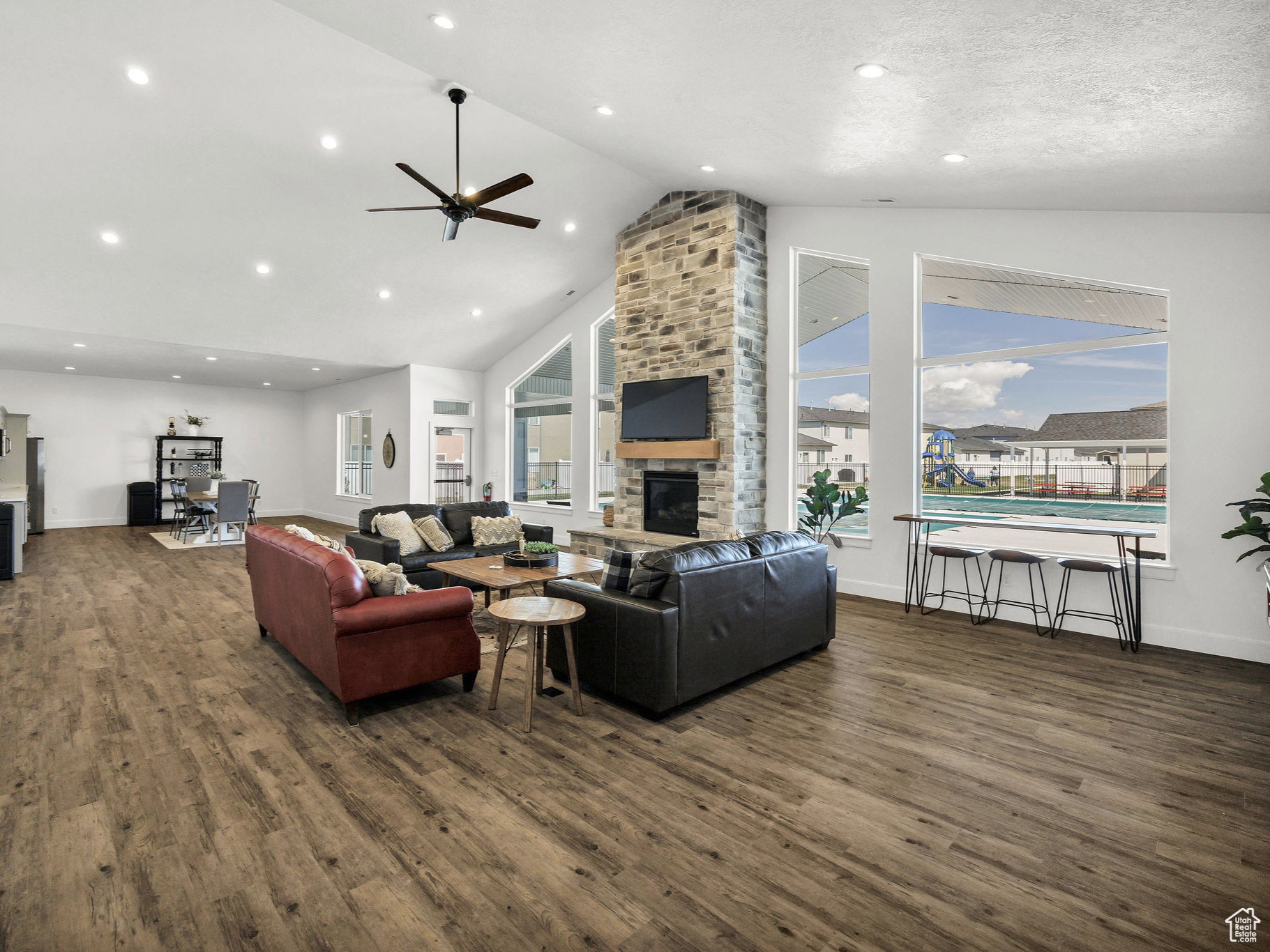 Living room with a fireplace, dark wood finished floors, ceiling fan, a high ceiling, and recessed lighting