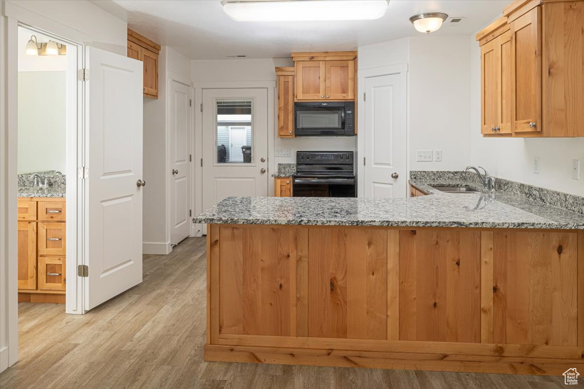 Kitchen with light stone counters, a peninsula, black appliances, and light wood-style flooring