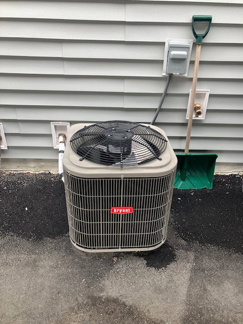 Bryant air conditioning unit positioned on a paved surface alongside light gray horizontal siding