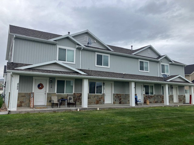 Multi-unit building featuring light gray vertical siding, stone veneer accents, white trim, and dark shingle roofing
