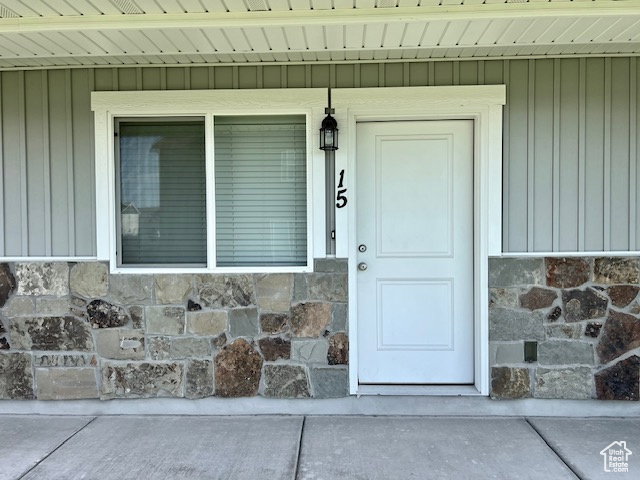 View of exterior entry featuring a porch, stone siding, and board and batten siding