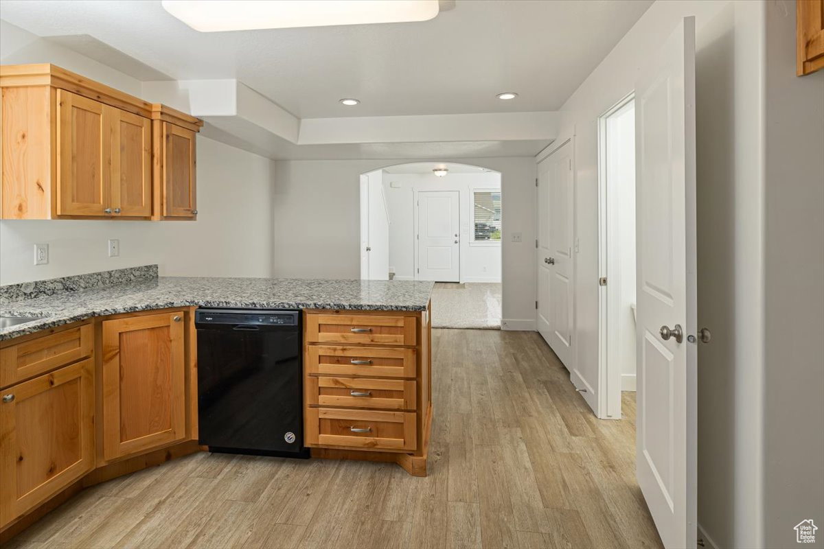 Kitchen featuring light wood-style flooring, a peninsula, light stone countertops, black dishwasher, and arched walkways