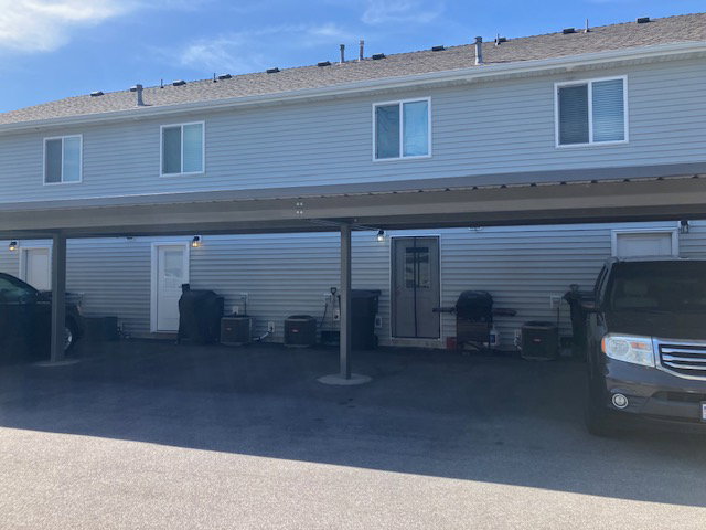 Rear exterior of a multi-unit property featuring light gray horizontal siding and a dark shingle roof