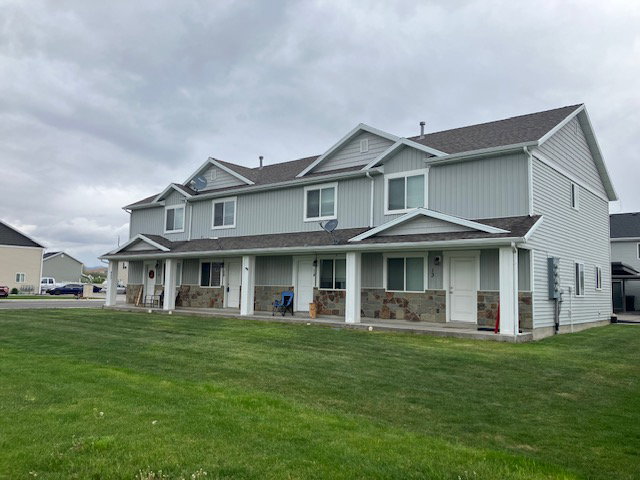 Multi-unit property featuring light grey vertical and horizontal siding, stone veneer accents, white trim, and a dark shingle roof