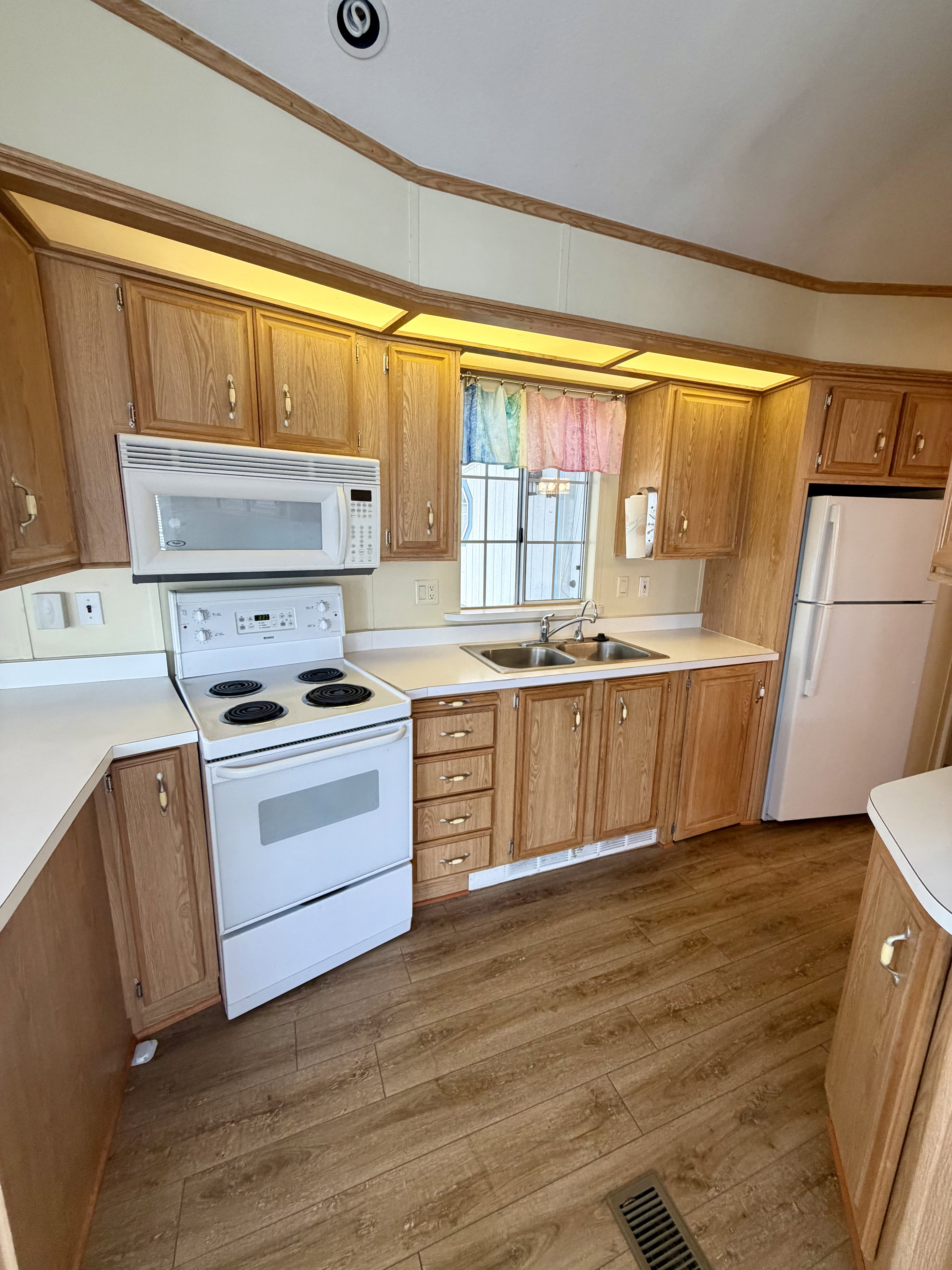 Kitchen with light countertops, white appliances, ornamental molding, light wood finished floors, and wood finish cabinets