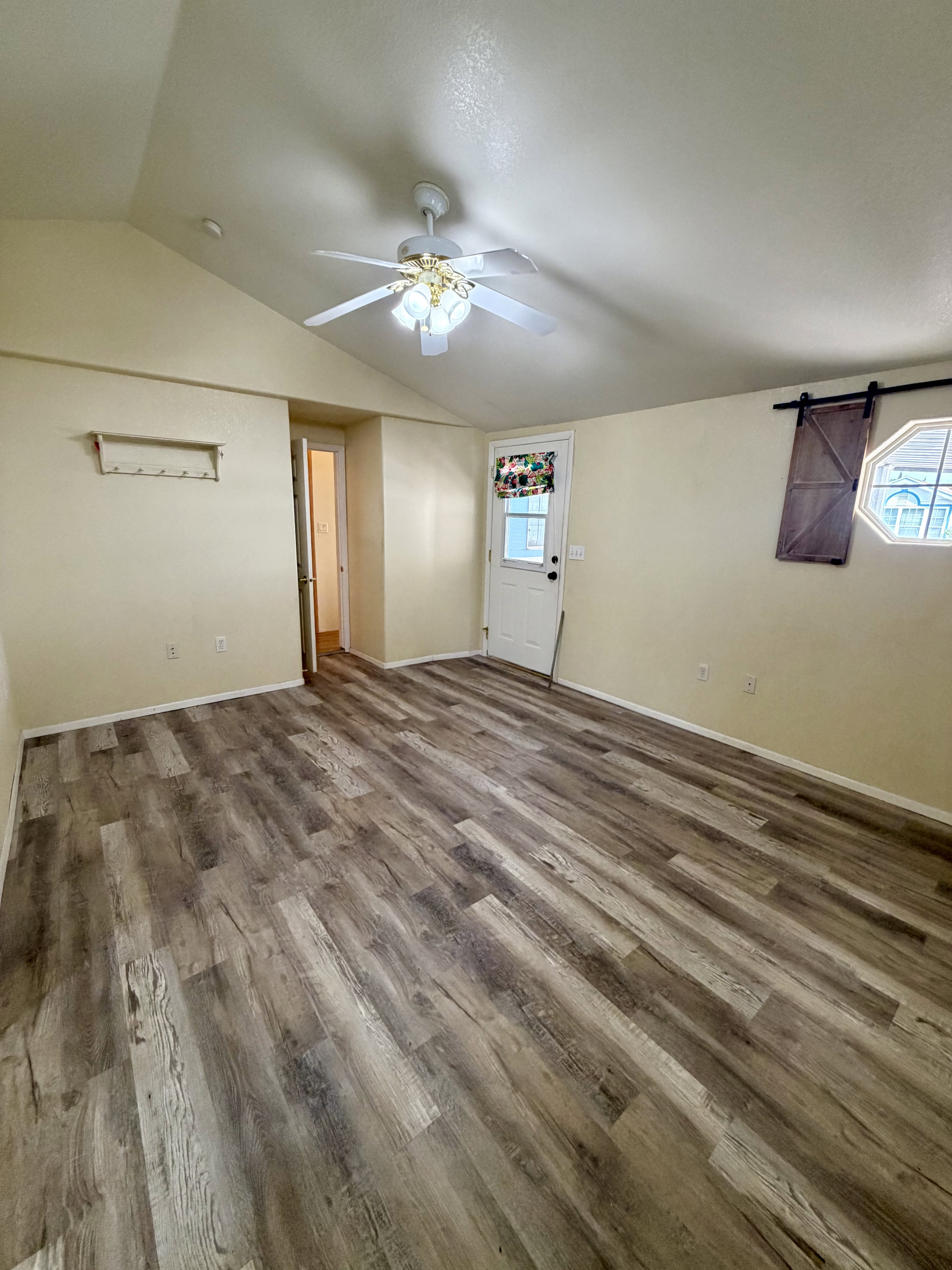 Unfurnished living room featuring a barn door, dark wood finished floors, ceiling fan, and healthy amount of natural light