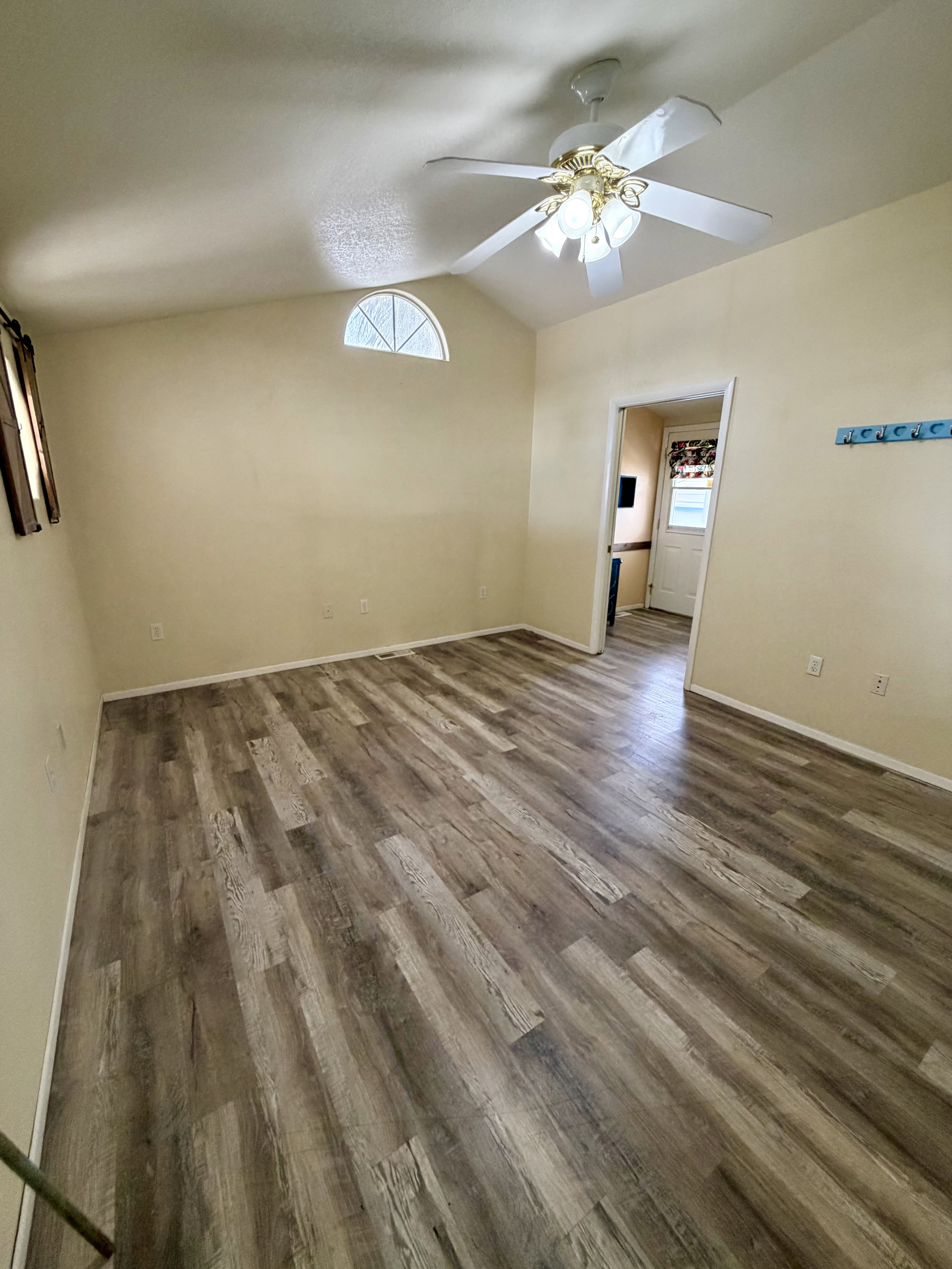 Empty room featuring dark wood finished floors, ceiling fan, and vaulted ceiling
