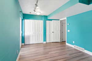 Unfurnished bedroom featuring light wood-style floors, multiple closets, a textured ceiling, and rail lighting
