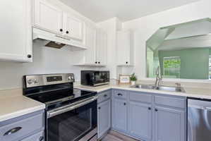 Kitchen with stainless steel appliances, light countertops, dual tone cabinets, and light wood-style flooring