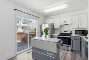 Kitchen with stainless steel appliances, light countertops, a center island, light wood-style flooring, and dual tone cabinetry
