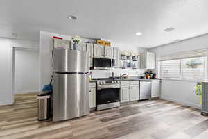 Kitchen with stainless steel appliances, dark countertops, light wood-style flooring, open shelves, and recessed lighting