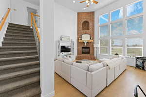 Living area with a high ceiling, ceiling fan, light wood-style flooring, a fireplace, and plenty of natural light