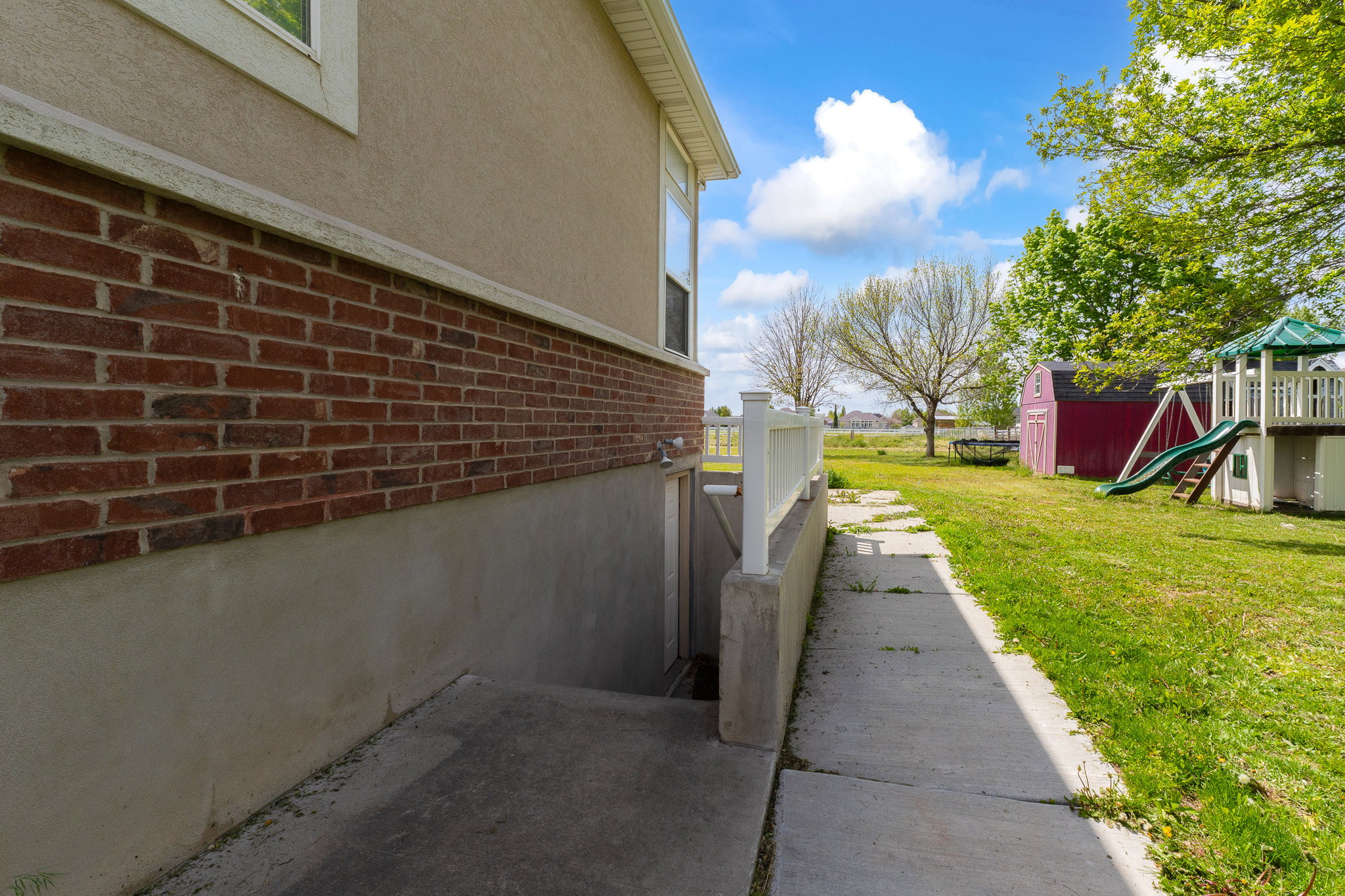View of side of home with brick siding, a playground, a shed, a yard, and stucco siding