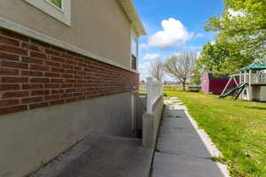 View of side of home with brick siding, a playground, a shed, a yard, and stucco siding