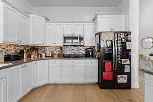 Kitchen with black fridge with ice dispenser, white cabinets, and dark countertops