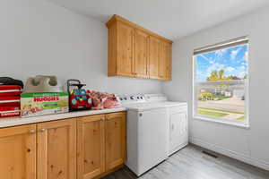 Laundry room with cabinet space, washing machine and dryer, and light wood-style floors