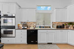 Kitchen featuring double oven, white cabinets, black dishwasher, and healthy amount of natural light