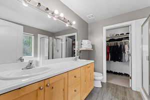 Bathroom featuring a shower stall, double vanity, a walk in closet, and dark wood-style floors