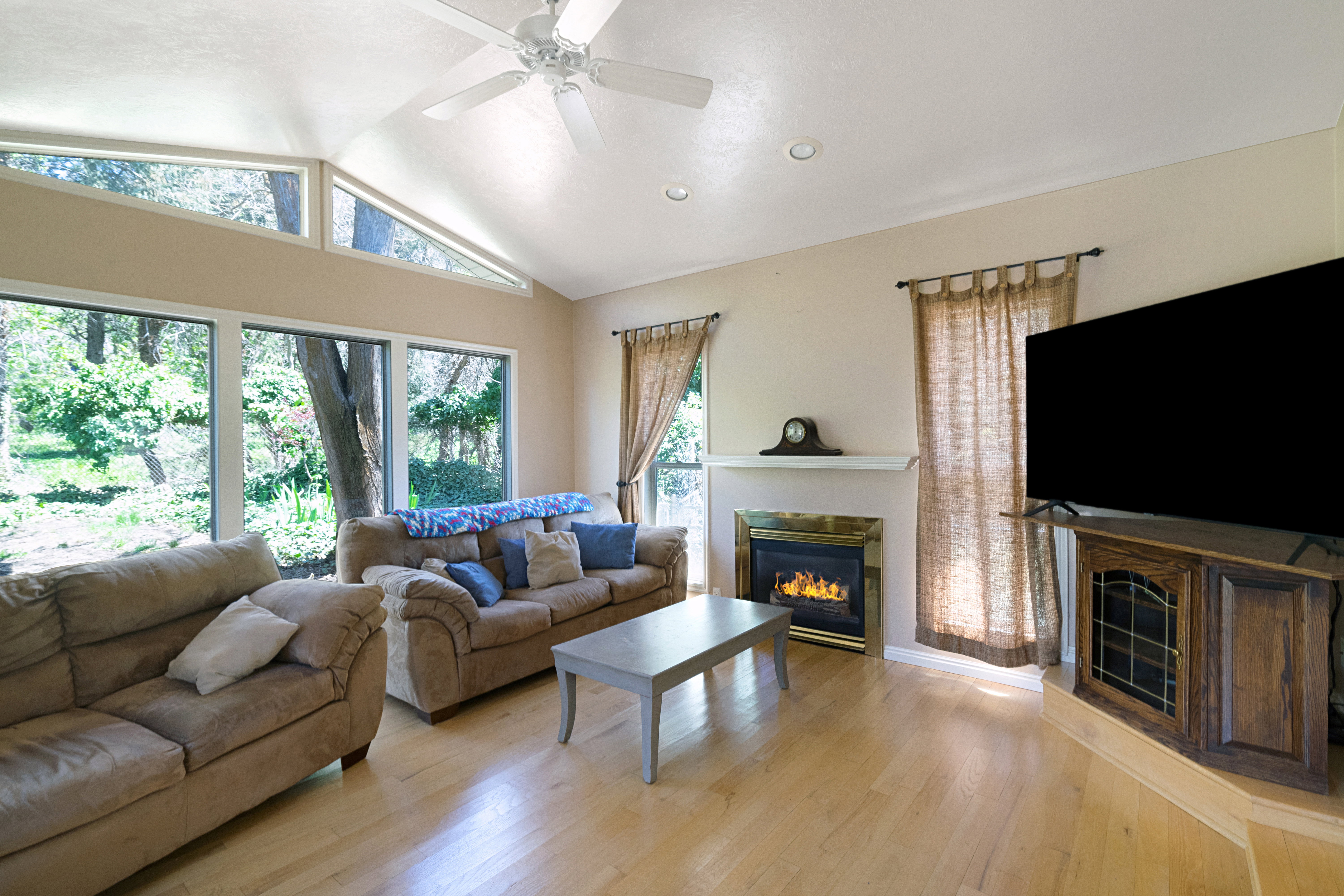 Living room with a glass covered fireplace, a ceiling fan, and light wood-style flooring