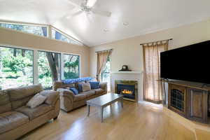 Living room with a glass covered fireplace, a ceiling fan, and light wood-style flooring
