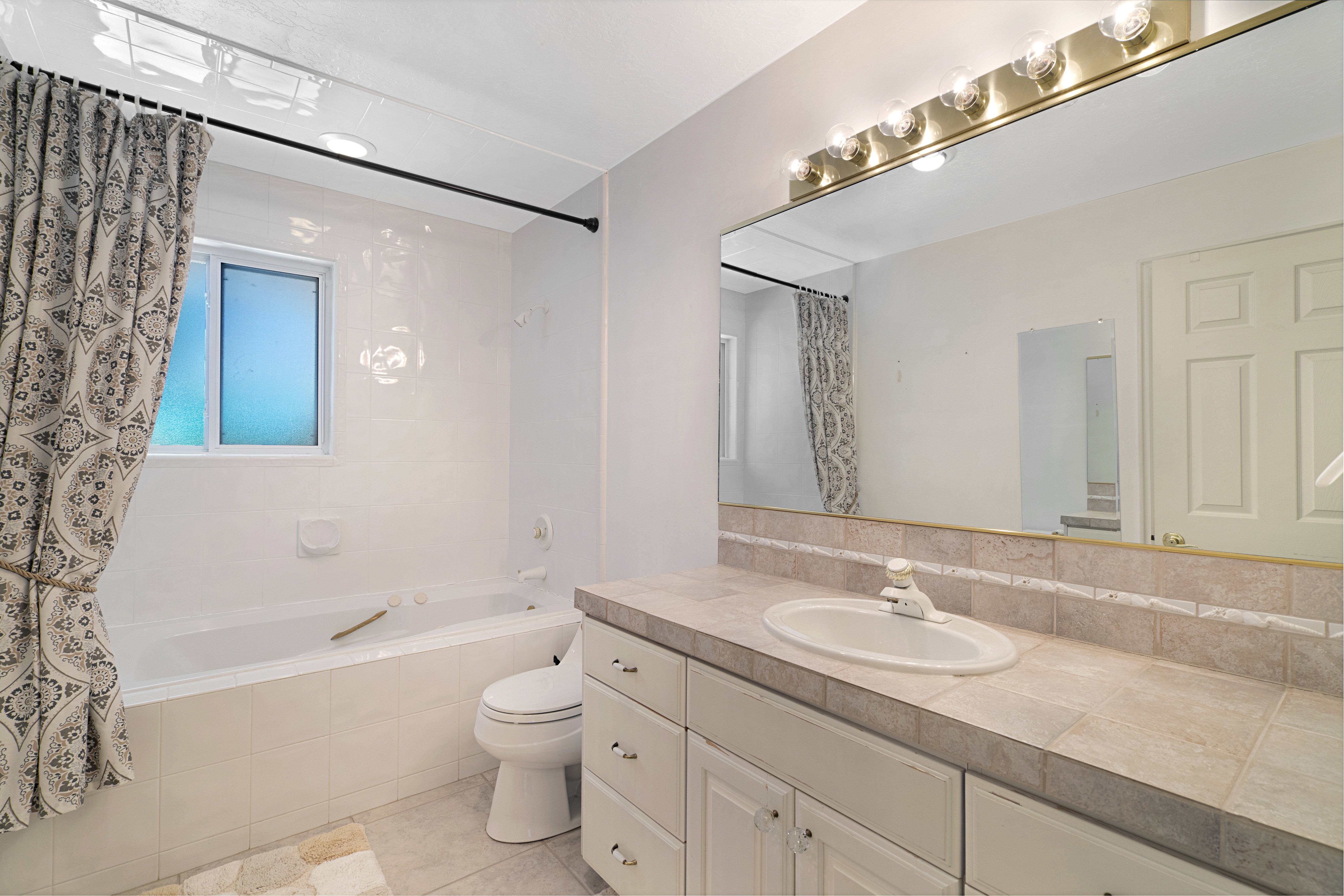Bathroom with tiled shower / bath combo, vanity, and light tile patterned flooring