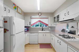 Kitchen with white appliances, light countertops, light wood-type flooring, white cabinetry, and glass fronted cabinets