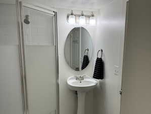 Shower bath with a pedestal sink, brushed nickel lighting fixture, and a tiled shower with a glass enclosure