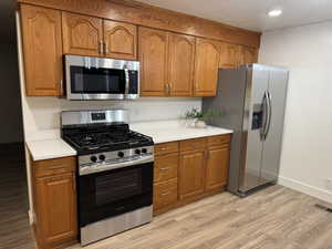 Kitchen featuring wood cabinetry, stainless steel appliances, white countertops, and wood-finish flooring