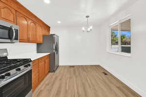 Kitchen with stainless steel appliances, light wood-style floors, hanging lights, and wood finish cabinets
