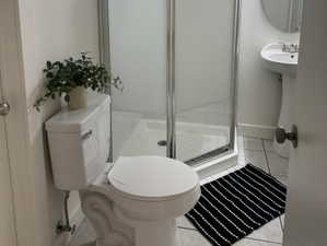 Bathroom featuring a corner glass-enclosed shower with subway tile surround, pedestal sink, and circular mirror