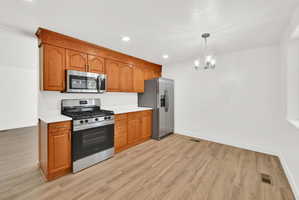 Kitchen with stainless steel appliances, wood finish cabinets, light countertops, light wood-style flooring, and a chandelier