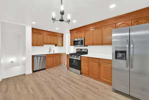 Kitchen featuring stainless steel appliances, light countertops, wood finish cabinets, light wood finished floors, and suspended lighting