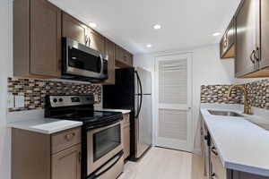 Kitchen featuring wood-finish cabinetry, stainless steel appliances, mosaic tile backsplash, white countertops, and recessed lighting