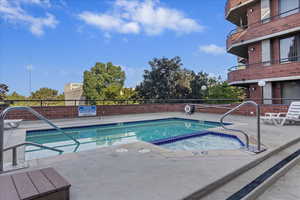 Rooftop pool and hot tub area featuring concrete decking, brick perimeter wall, and surrounding building with brick exterior