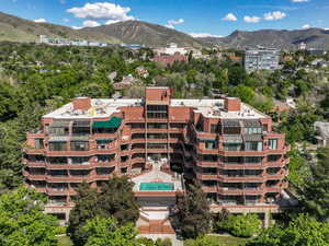 Multi-story brick facade building featuring tiered balconies, an outdoor swimming pool, and surrounding mature trees