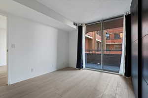 Sliding glass doors opening to a private balcony, light wood-finish flooring, white walls, and a dark paneled accent wall