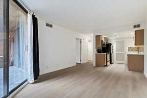 Open-concept living space featuring wood-finish flooring throughout, a full kitchen with brown cabinetry and mosaic tile backsplash, and a sliding glass door leading to an outdoor area