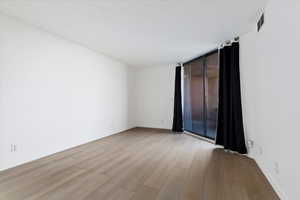 Light wood-finish flooring complements the bright white walls of this room, featuring a large glass sliding door with dark drapes